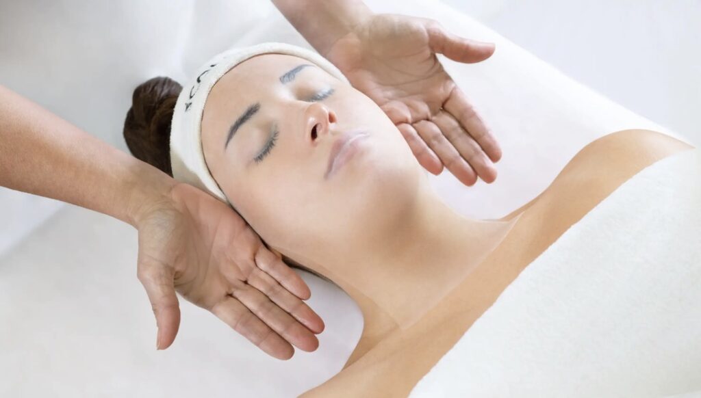 GM Collin relaxing facial massage technique performed by esthetician with hands gently positioned around client's face and neck during a professional spa facial