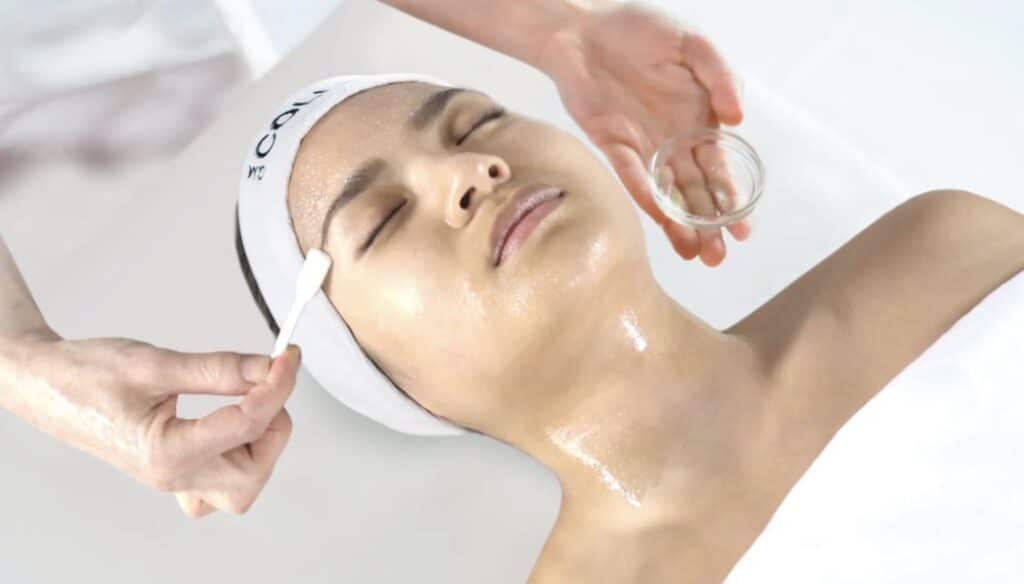 GM Collin facial treatment with esthetician applying professional serum using a brush on a client's face during a luxury spa facial