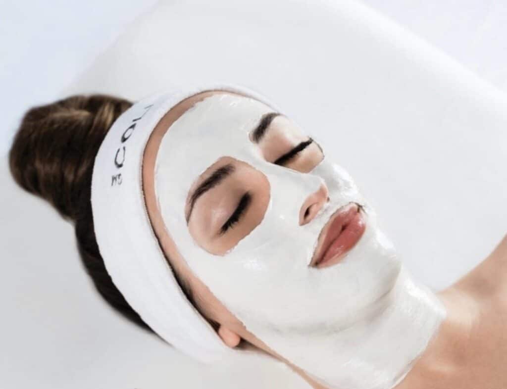GM Collins Pro facial treatment with white clay mask applied to woman's face wearing spa headband